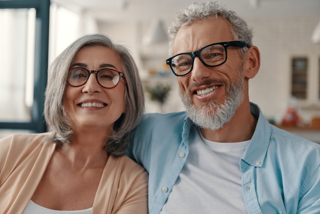 Smiling senior couple wearing glasses sitting together at home