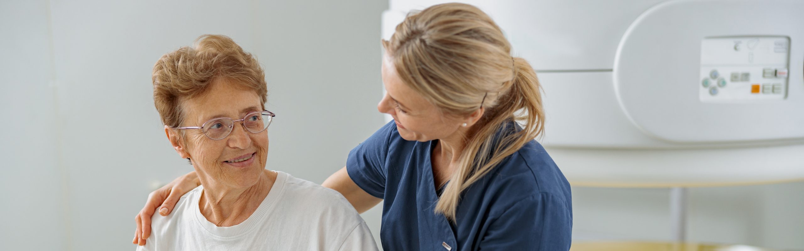 Healthcare provider with a hand on an elderly patient's shoulder near a medical imaging machine