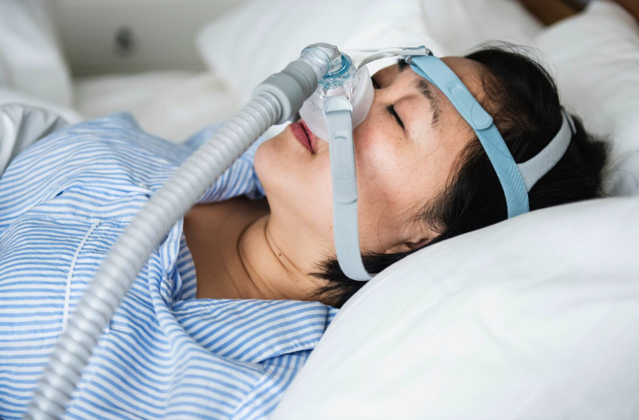 Woman sleeping in bed while wearing a CPAP mask for sleep apnea treatment