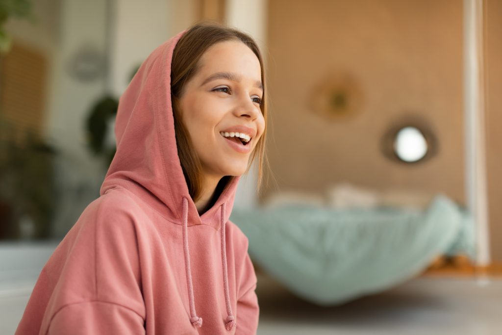 Teenage girl in a pink hoodie smiling at home