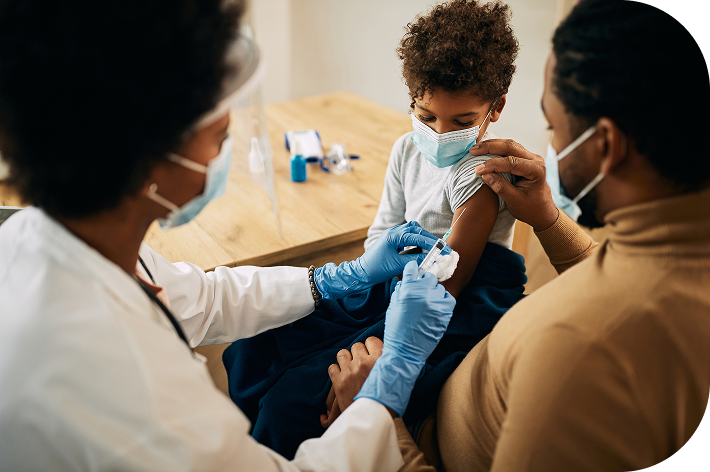 Doctor administering a vaccine injection to a young boy's arm while his father holds him