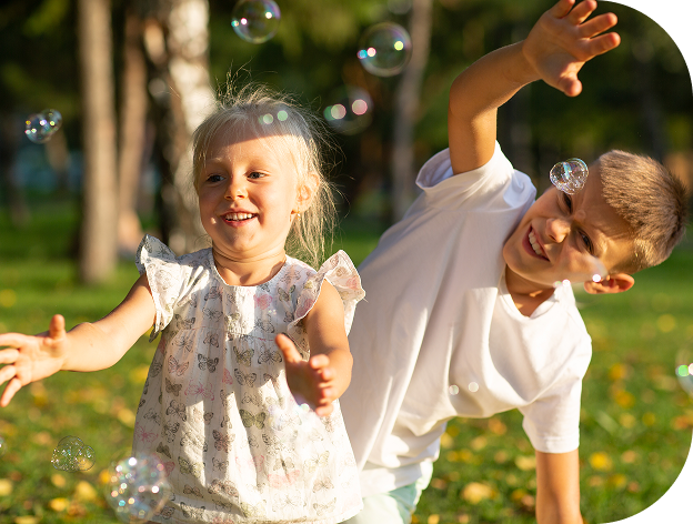 Two children playing outdoors and chasing soap bubbles in a park
