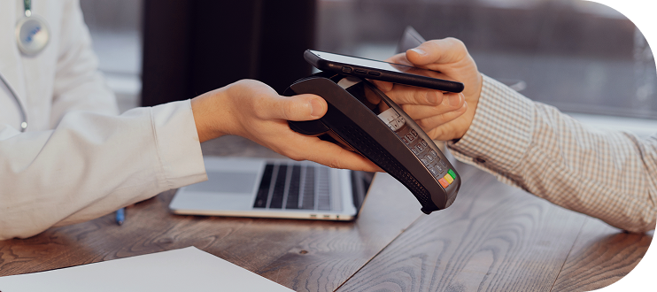 Patient making a contactless payment on a card reader held by a healthcare provider