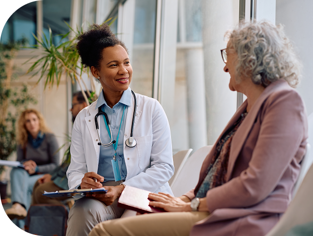 Doctor talking with an older woman patient in a waiting room while taking notes