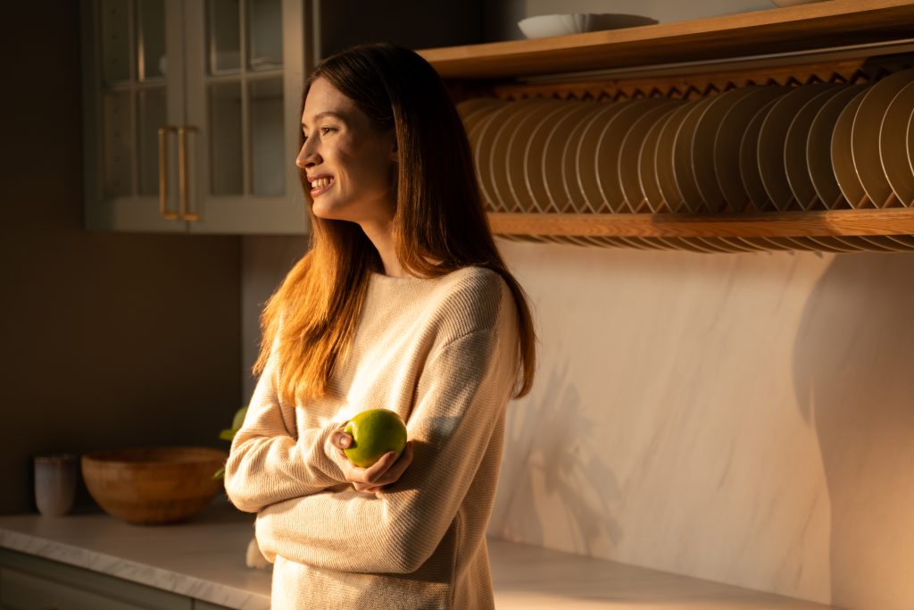 Woman smiling in a sunlit kitchen holding an apple