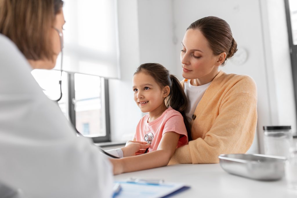 Doctor examining a young girl with a stethoscope while her mother sits beside her